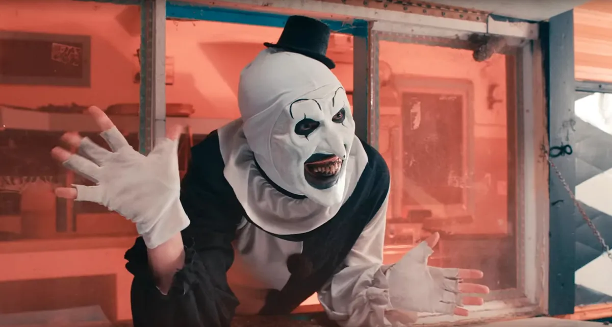 Art the Clown from the Terrifier movies, with his signature sinister smile and black and white makeup, holding a weapon.