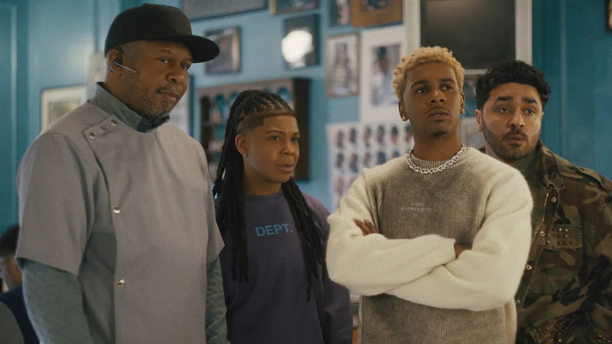 Jermaine Fowler looking slightly overwhelmed but determined in a lively barbershop scene.