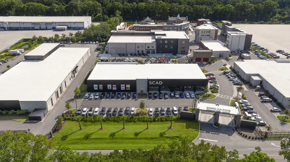 An aerial view of the expanded SCAD Film Studios backlot with new soundstages and various film set facades under a sunny sky.