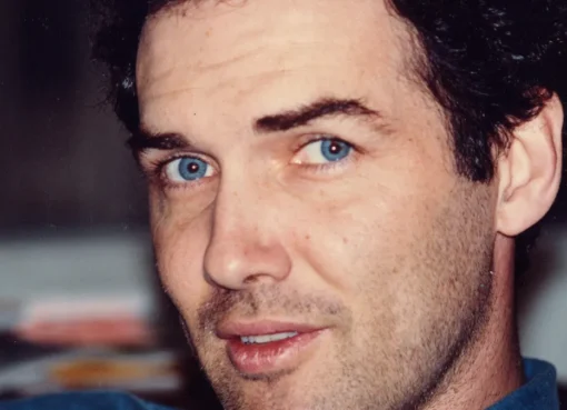A close-up photo of Norm MacDonald with a thoughtful and slightly mischievous expression.