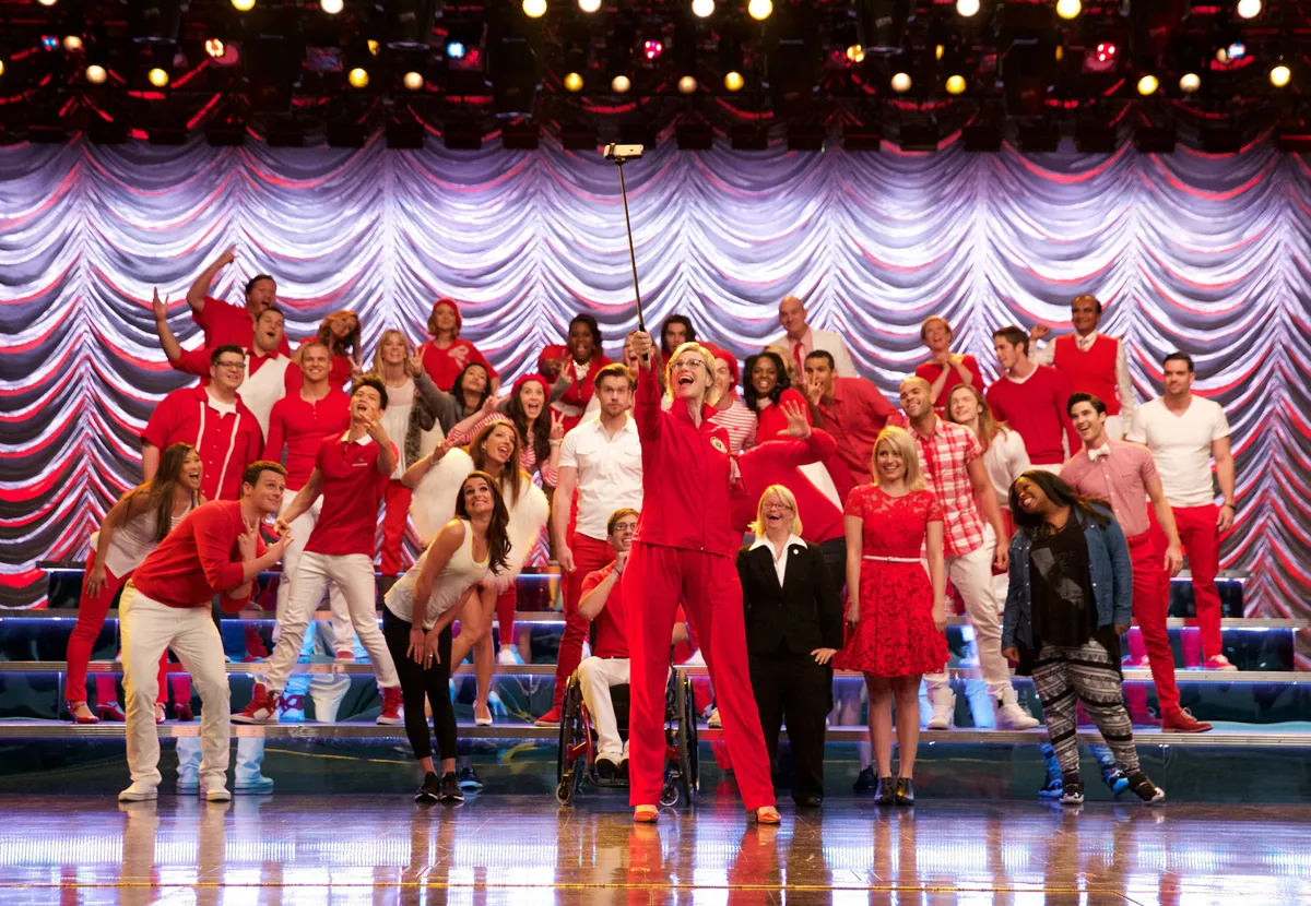 A group of happy young people singing and dancing on stage, similar to the cast of Glee.