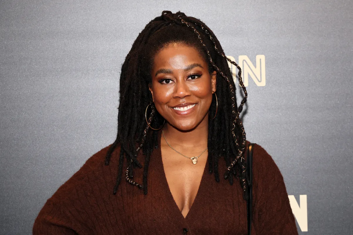Tomi Adeyemi smiling and holding a copy of her book at an event.