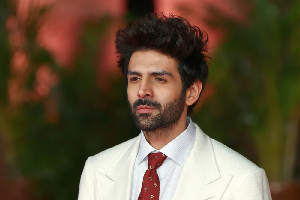 Kartik Aaryan looking serious in a pilot's uniform, possibly against a dramatic, dusty background.