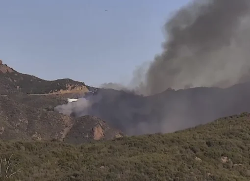 Smoke rising from a wildfire in a dry, hilly area.