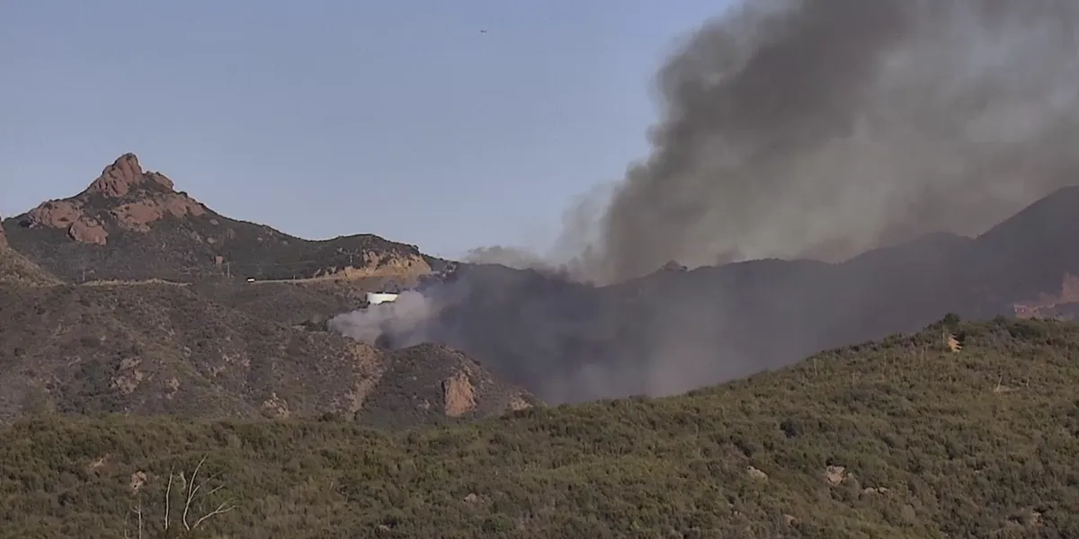 Smoke rising from a wildfire in a dry, hilly area.