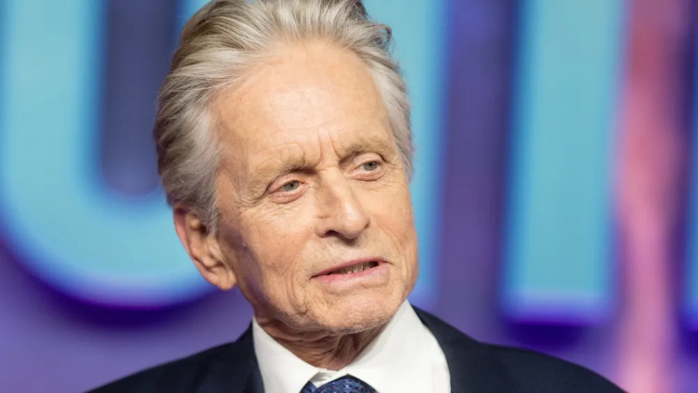 Michael Douglas smiling during an interview, wearing a dark suit.