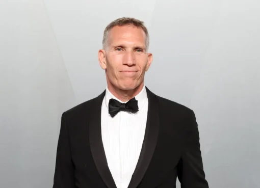 A man in a suit smiling confidently, likely in a corporate setting.
