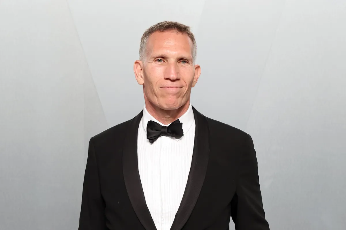 A man in a suit smiling confidently, likely in a corporate setting.