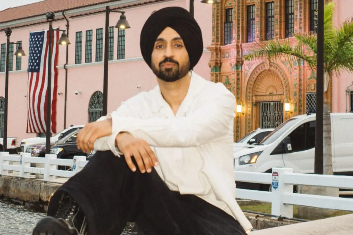Diljit Dosanjh performing on stage under bright, colourful lights.